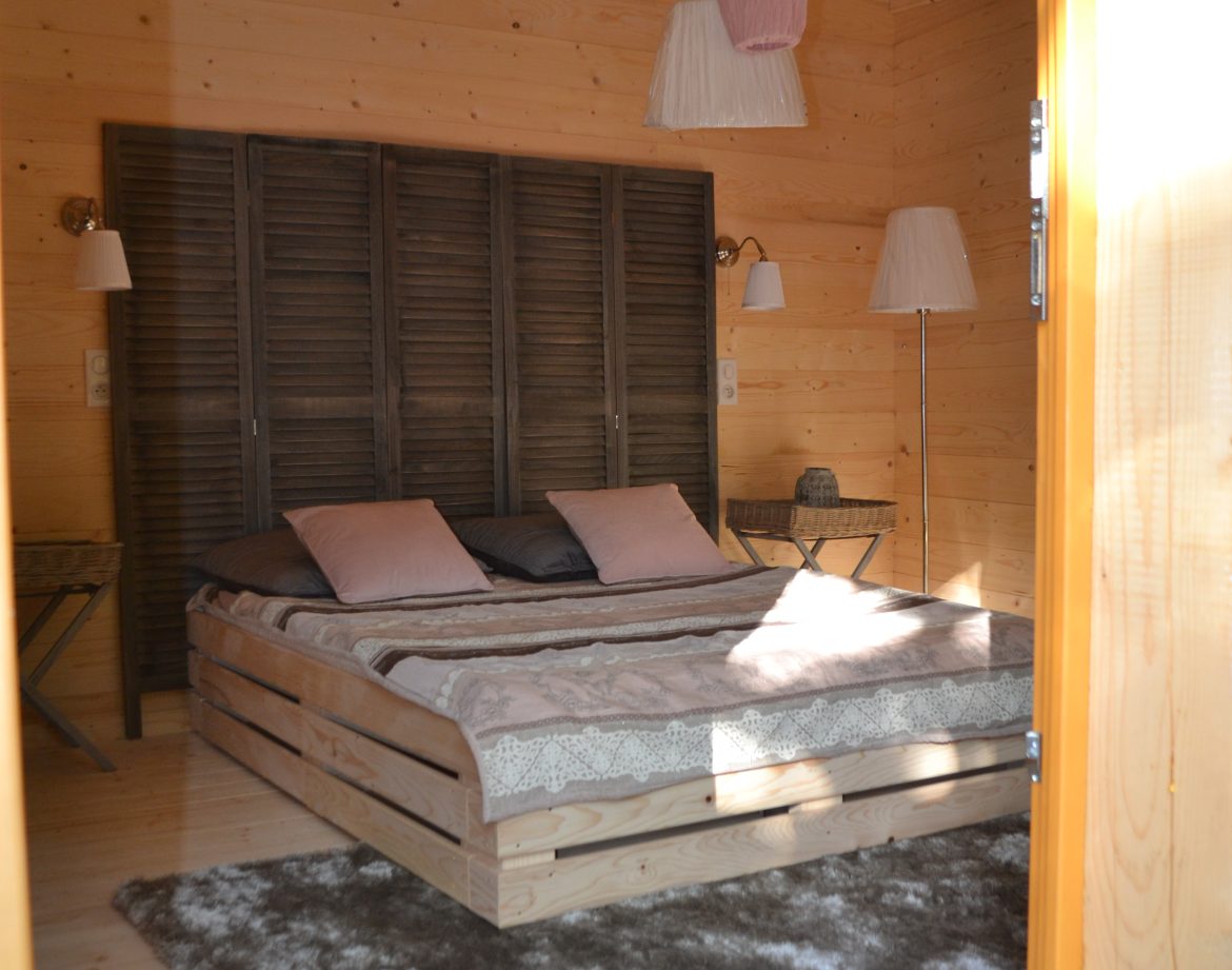 Chalet en bois à Nouvelle-Aquitaine, intérieur cosy avec lit en palette et tapis moelleux.