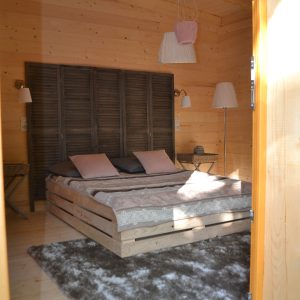 Chalet en bois à Nouvelle-Aquitaine, intérieur cosy avec lit en palette et tapis moelleux.