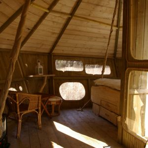 Cabane perchée en bois avec fenêtres rondes et mobilier en rotin. Ambiance chaleureuse.