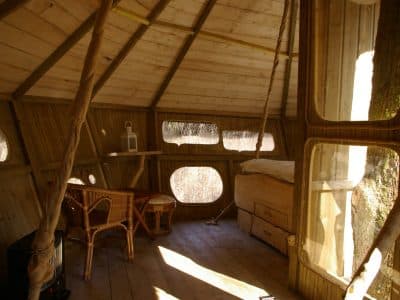 Cabane perchée en bois avec fenêtres rondes et mobilier en rotin. Ambiance chaleureuse.