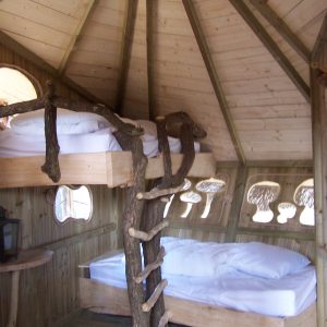 Cabane en bois avec lits superposés et échelle en branches, ambiance naturelle.
