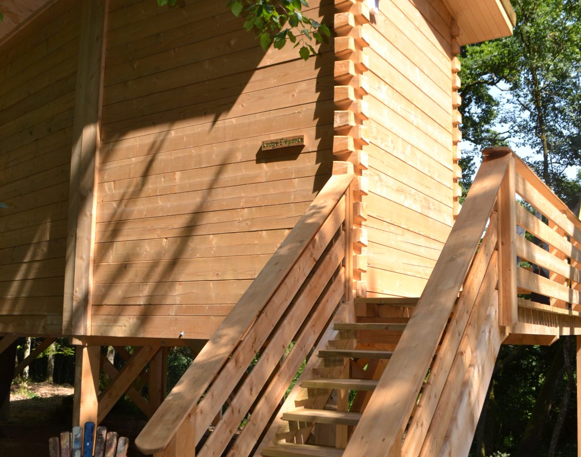 Cabane en bois sur pilotis, avec un escalier en bois et un coin détente à lextérieur.