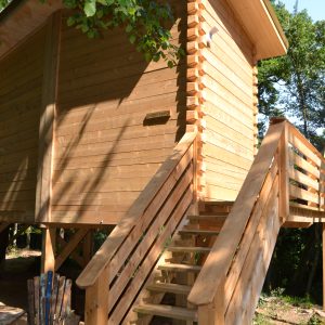Cabane en bois sur pilotis, avec un escalier en bois et un coin détente à lextérieur.