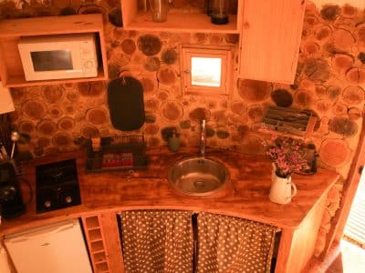 Hébergement insolite en Aquitaine : cuisine en bois avec murs en rondins et lumière naturelle.