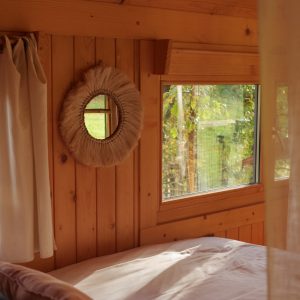 Cabane en bois avec un lit douillet et une fenêtre offrant une vue sur la nature.