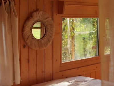 Cabane en bois avec un lit douillet et une fenêtre offrant une vue sur la nature.