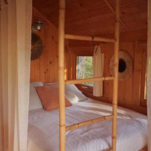 Cabane en bois dans les arbres, lit douillet et échelle en bambou.