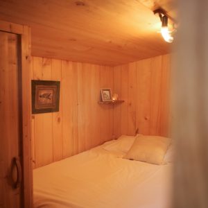 Cabane en bois chaleureuse avec lit douillet et ambiance lumineuse apaisante.