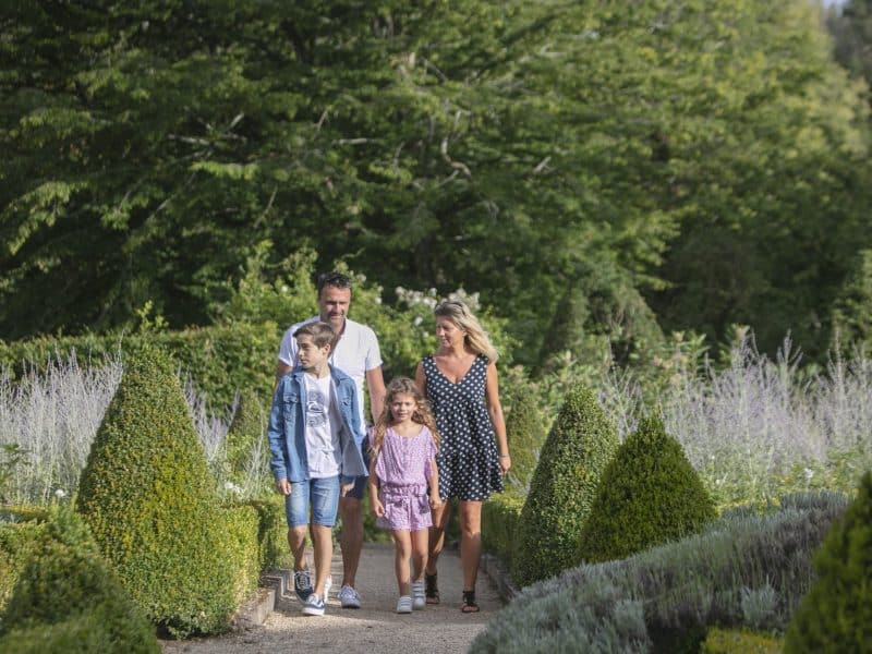 Famille se promenant dans un jardin dun gîte rural, entourée de verdure.