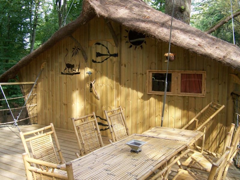 Cabane en bois dans les arbres avec terrasse en bambou et décorations naturelles.