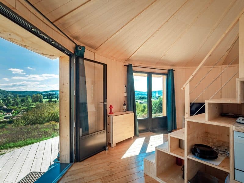 Cabane moderne avec vue panoramique, intérieur en bois clair et cuisine équipée.