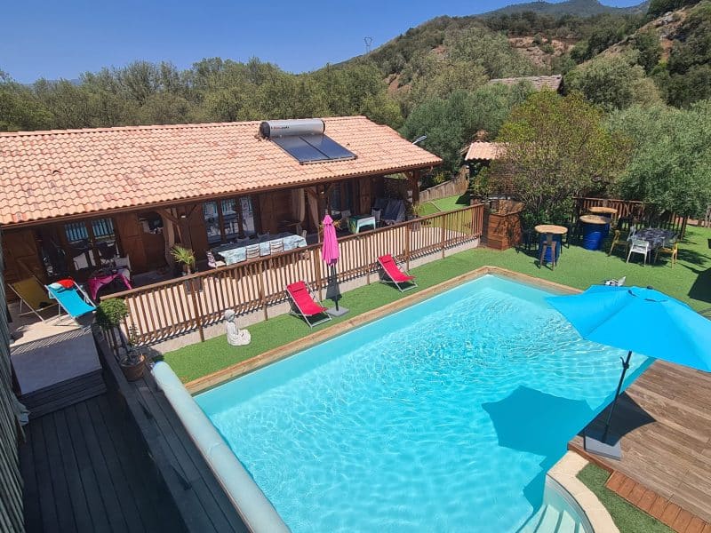 Chalet avec piscine, transats et parasol, entouré de verdure. Détente assurée !