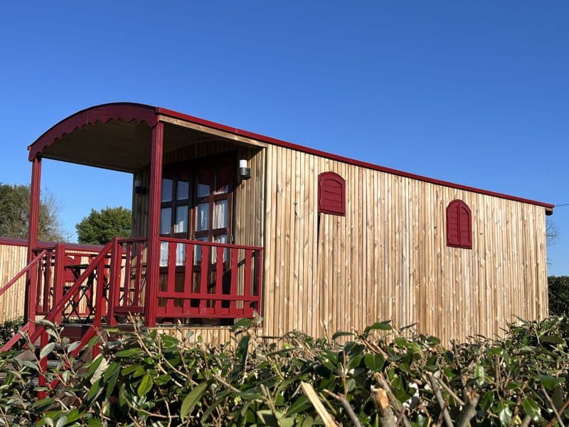 Chalet en bois avec balustrade rouge, entouré de verdure sous un ciel bleu.