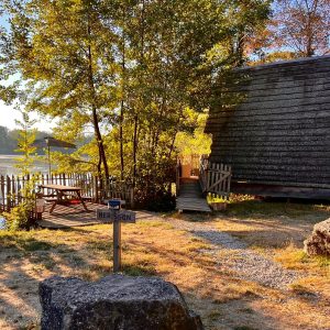 Cabane en bois au bord dun lac, entourée darbres et dune terrasse ensoleillée.