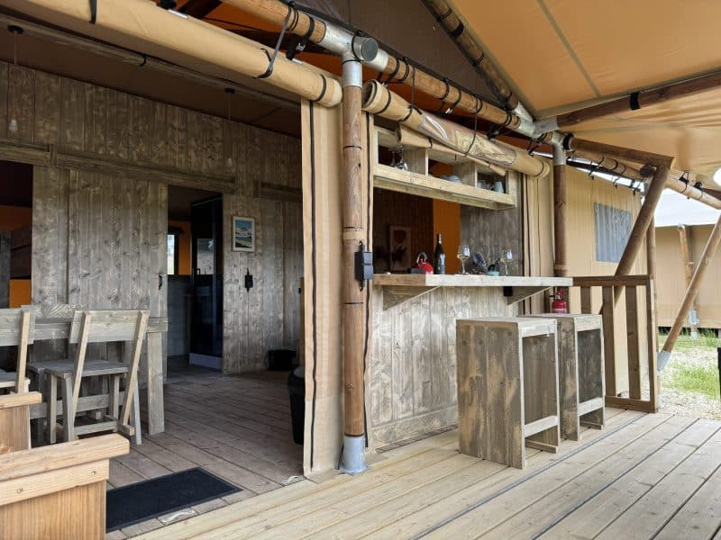 Tente safari avec terrasse en bois, bar extérieur et ambiance chaleureuse.