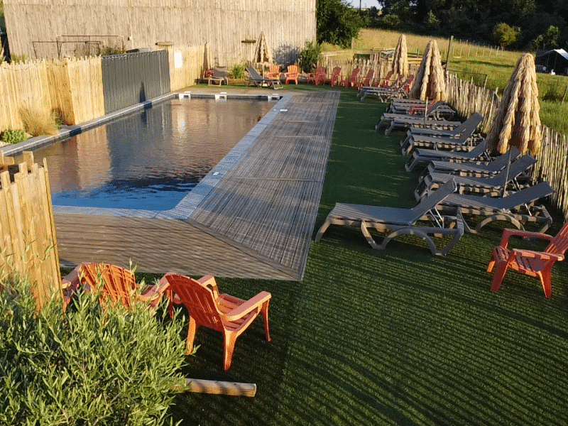 Hébergement en plein air avec piscine, chaises longues colorées et espace verdoyant.