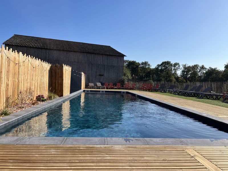 Gîte avec piscine extérieure, entouré de chaises longues et dun cadre verdoyant.