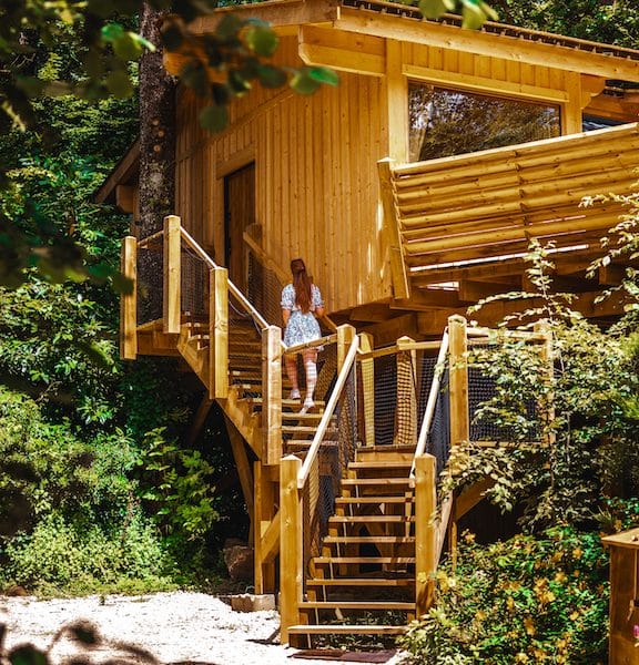 Cabane en bois perchée dans les arbres, entourée de verdure luxuriante.