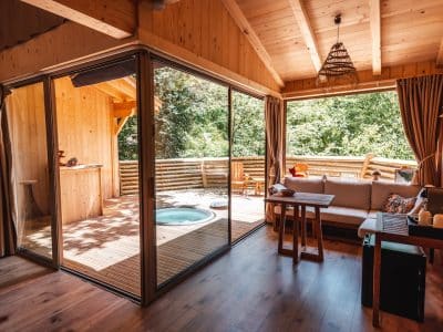 Cabane en bois avec jacuzzi, baignée de lumière naturelle et vue sur la nature.