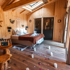 Chalet en bois chaleureux avec lit douillet et pétales de fleurs au sol.