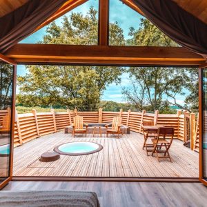 Cabane en bois avec terrasse en bois et jacuzzi, vue sur la nature.