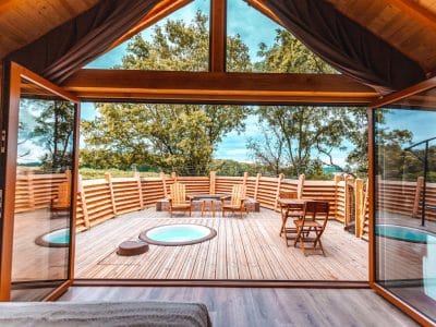 Cabane en bois avec terrasse en bois et jacuzzi, vue sur la nature.