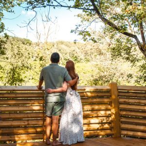 Cabane perchée dans les arbres, couple admirant la vue verdoyante.