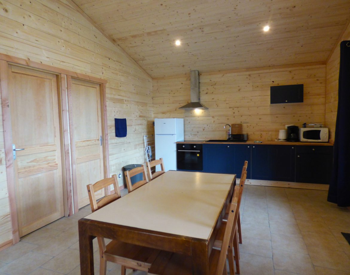Chalet en bois à Auvergne, intérieur lumineux avec cuisine moderne et table en bois.