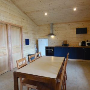 Chalet en bois à Auvergne, intérieur lumineux avec cuisine moderne et table en bois.