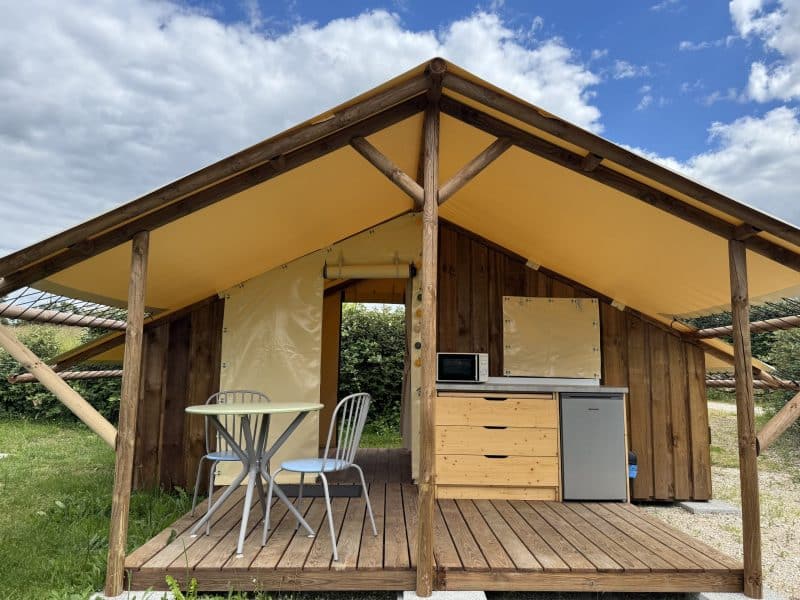 Cabane en bois avec terrasse, kitchenette et ciel bleu en arrière-plan.