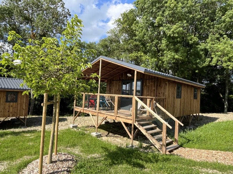 Cabane en bois avec terrasse, entourée de verdure et darbres. Parfait pour se détendre.