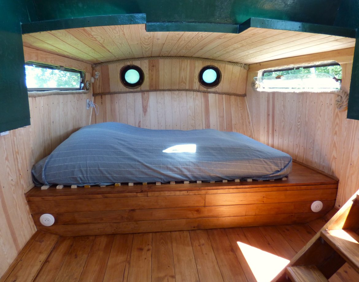 Hébergement insolite en Auvergne : cabane avec lit en bois et fenêtres rondes.