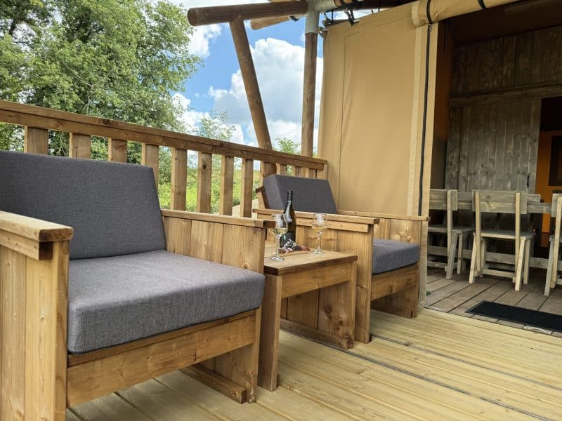 Tente safari avec terrasse en bois, chaises confortables et vue sur la nature.