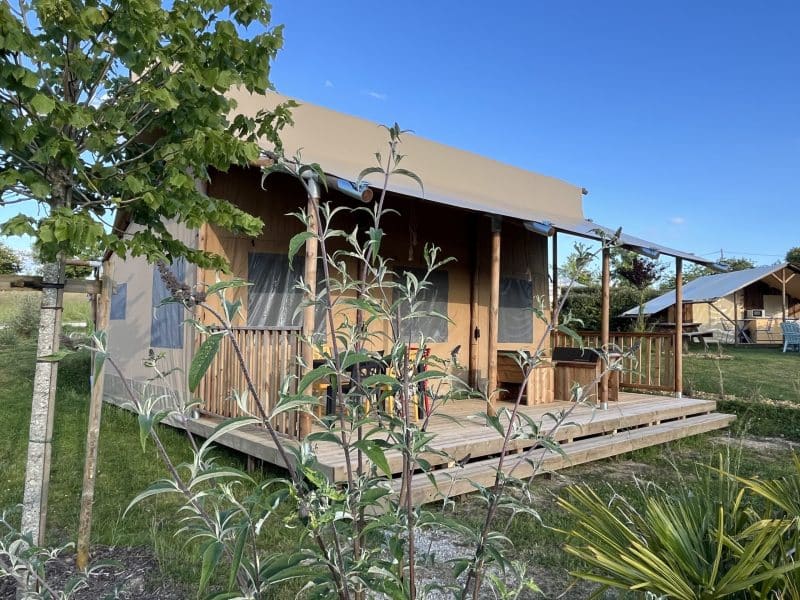 Tente safari spacieuse avec terrasse en bois, entourée de verdure.