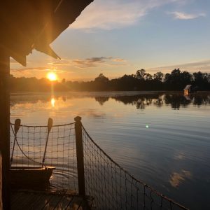 Cabane flottante au bord dun lac, avec un coucher de soleil éclatant.
