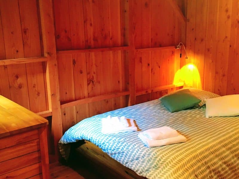 Chalet en bois chaleureux avec lit douillet et linge de lit soigné.