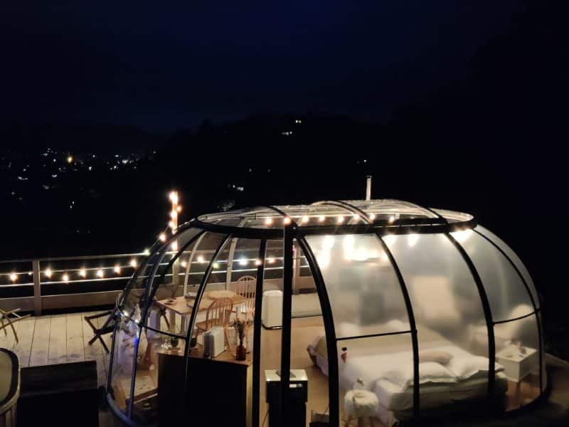 Hébergement insolite : bulle transparente illuminée, vue sur la ville nocturne.