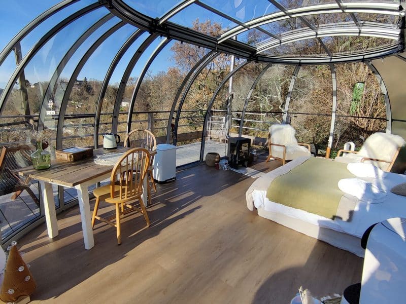 Dôme transparent avec lit confortable et coin repas, offrant une vue panoramique.