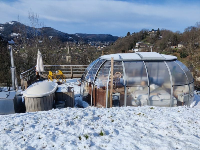 Hébergement insolite : bulle transparente avec jacuzzi, vue sur la montagne enneigée.