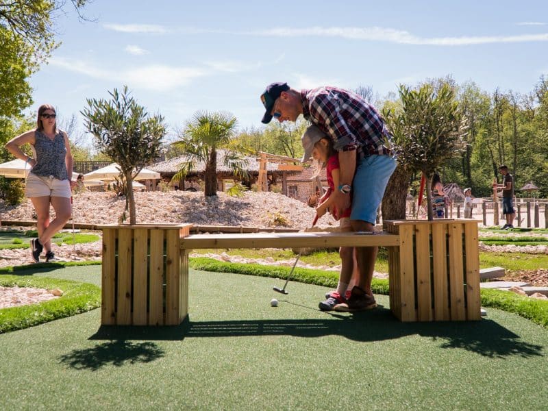 Mini-golf en plein air, famille samusant sur un parcours verdoyant et ensoleillé.