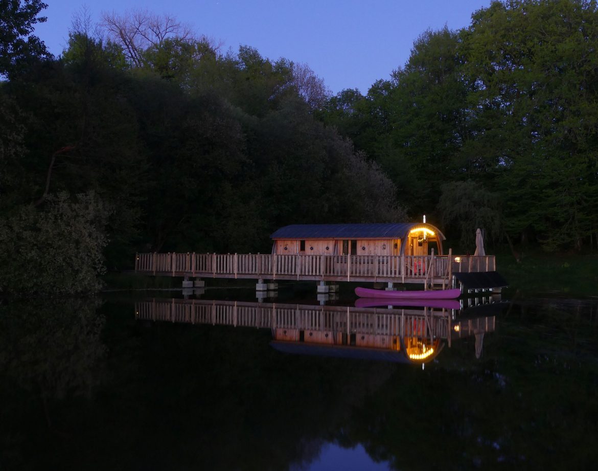 Cabane flottante au Limousin, illuminée, reflétée sur leau paisible.