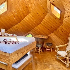 Cabane en bois avec lit douillet, fenêtres lumineuses et décoration romantique.