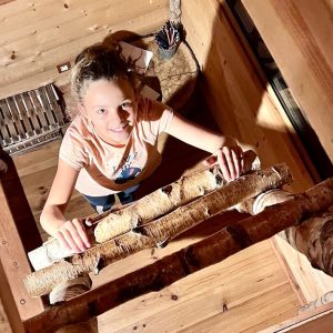 Cabane en bois dans les arbres, avec une échelle en rondins et une vue intérieure chaleureuse.