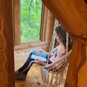 Cabane perchée en Auvergne-Rhône-Alpes, enfant lisant dans un hamac suspendu.