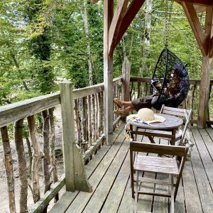 Hébergement insolite en cabane perchée, avec un fauteuil suspendu et vue sur la forêt.