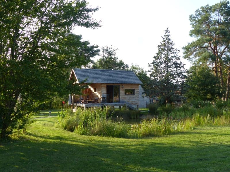 Chalet en bois au bord dun étang, entouré de verdure luxuriante.