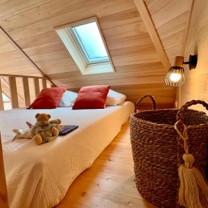Chalet en bois avec lit douillet, éclairage chaleureux et vue sur le ciel.