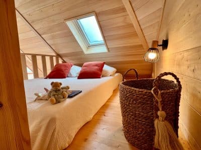 Chalet en bois avec lit douillet, éclairage chaleureux et vue sur le ciel.