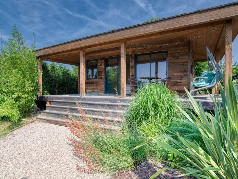 Cabane en bois avec terrasse, entourée de verdure luxuriante à Languedoc-Roussillon.
