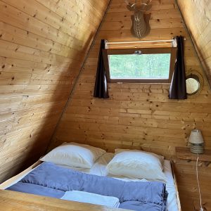 Cabane en bois à la forme triangulaire, avec un lit douillet et des murs en bois.